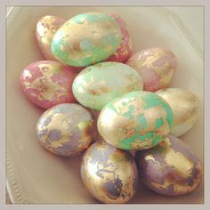 a bowl filled with gold and green painted eggs on top of a white tablecloth