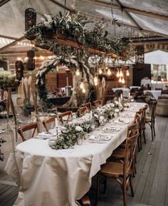 a long table is set up with white linens and greenery