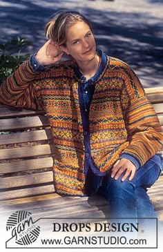 a man sitting on top of a wooden bench wearing a colorful cardigan and jeans