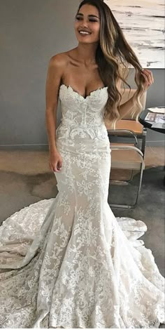 a woman in a white wedding dress standing next to a chair and looking at the camera