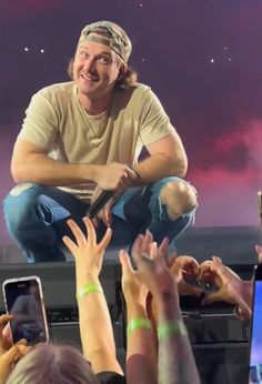 a man sitting on top of a stage surrounded by people holding their hands in the air