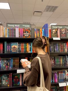 a woman standing in front of a bookshelf holding a book and looking at it