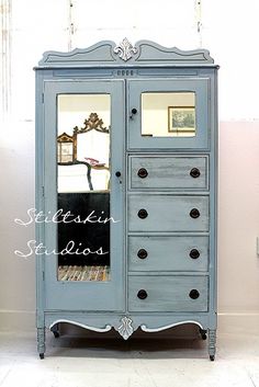 an antique blue armoire with mirrored doors and drawers in a room that has white walls