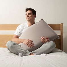 a man sitting on top of a bed holding a pillow