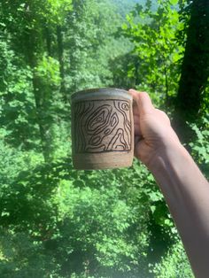 a person holding up a cup in front of a forest filled with lots of trees