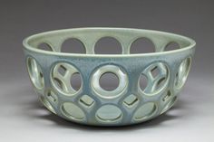 a blue bowl with circles and holes in the center on a gray background, sitting on top of a table