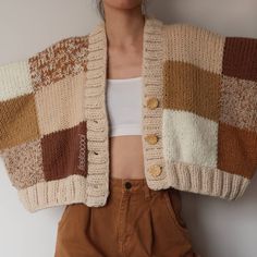 a woman is standing in front of a white wall wearing a sweater and brown pants