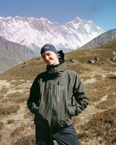 a man standing on top of a grass covered field next to mountains in the background