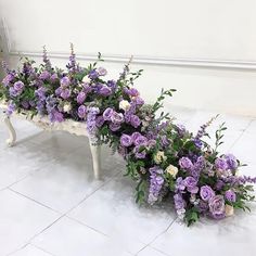 purple and white flowers are arranged on a bench in the middle of a tiled floor