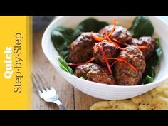 a white bowl filled with meatballs next to crackers and a fork on a wooden table