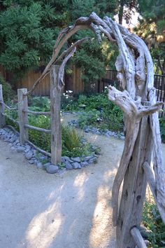 a wooden gate in the middle of a gravel area with rocks and plants around it