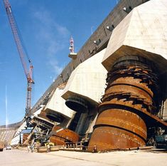 there are many large metal pipes in front of a building under construction with cranes on the other side