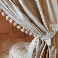 a white bed with pom poms on it's headboard and curtains