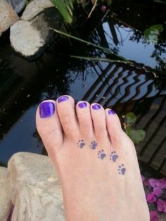 a person's foot with purple nail polish and paw prints on it next to a pond