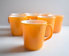 five orange coffee mugs lined up on a white counter top with one cup in the middle