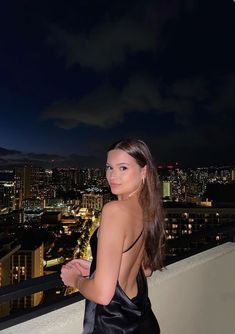 a beautiful young woman standing on top of a balcony next to a city at night