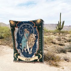 a blanket with a mermaid on it sitting in the middle of a dirt field next to a cactus