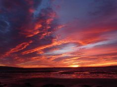 the sun is setting over the ocean with clouds in the sky