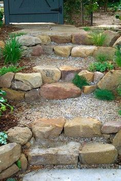 a stone path leading up to a blue door in the background with plants and rocks on either side