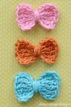 three crocheted bows are shown on a green surface, one is orange and the other is pink