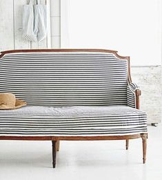 a striped couch sitting in front of a window next to a wooden table with a hat on it