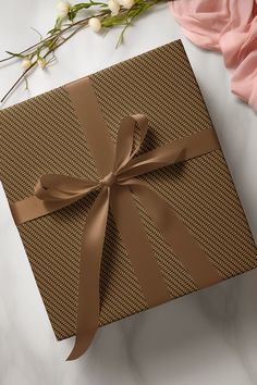 a brown gift box with a bow on top of it next to flowers and petals