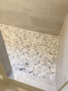 a walk in shower sitting next to a tiled wall and floor with pebbles on it