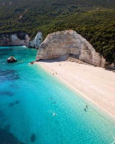 people are swimming in the clear blue water at an empty beach with cliffs on either side