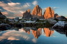 the mountain range is reflected in the still water at sunset, with rocks and grass on either side