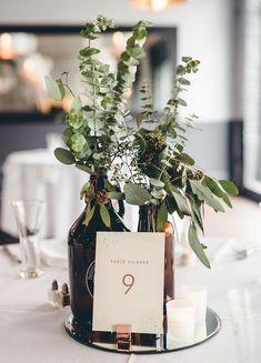 there is a vase with greenery in it and a table number on the plate