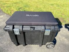 three black coolers sitting next to each other on top of a cement road near grass