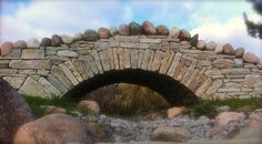 an old stone bridge built into the side of a hill with rocks and grass around it