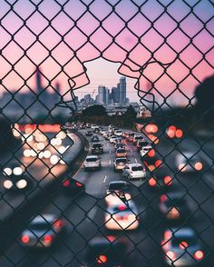 a view through a chain link fence at traffic on a busy highway with buildings in the background