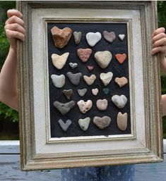 a person holding up a framed photo with rocks in the shape of hearts on it