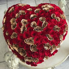 a heart shaped cake with red and gold roses on it's side sitting on a pedestal