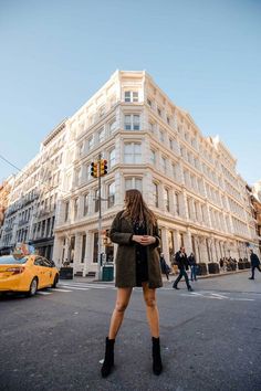 a woman standing on the street in front of a tall building with lots of windows