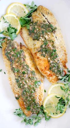 two fish fillets with herbs and lemons on a white plate