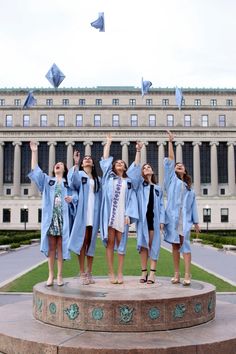 four girls in graduation gowns are standing on a pedestal and throwing their caps in the air