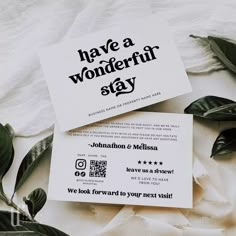 two business cards sitting on top of each other next to some leaves and white sheets