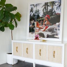 a white dresser with two drawers and a painting on the wall above it in a living room