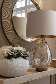 a table with a lamp, vase and mirror on it