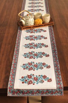 a table runner with tea pots and cups on it, sitting on top of a wooden table