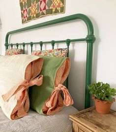 a bed with green headboard and pillows on top of it next to a potted plant