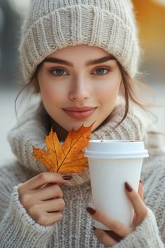 a young woman holding a cup of coffee and a leaf in her hand while wearing a knitted hat