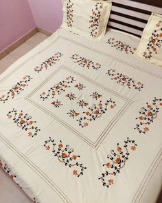 a white bed with orange and black embroidered flowers on it's sides, along with matching pillow cases