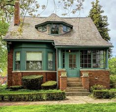 a small brick house with green trim and windows