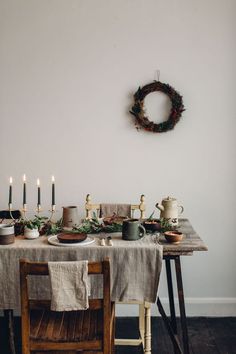 a dining room table with candles and plates on it, surrounded by greenery wreaths