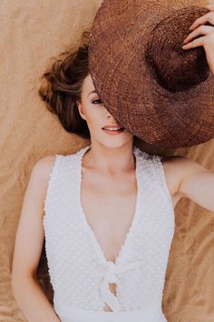 a woman laying on top of a bed wearing a brown and white hat over her head