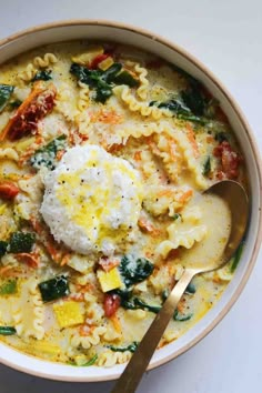 a bowl filled with pasta and spinach on top of a white table next to a spoon