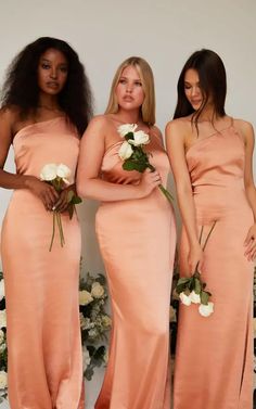 three beautiful women in long dresses standing next to each other with flowers on their bouquets